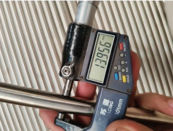 Digital micrometer measuring a polished metal rod during quality inspection