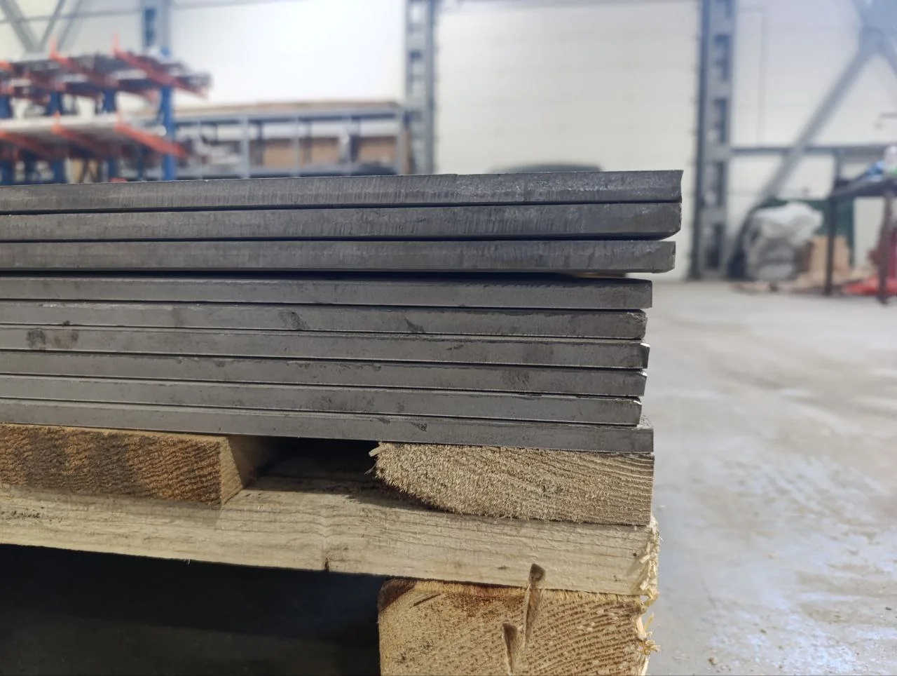 Heavy metal plate stock stacked on wooden supports in a workshop
